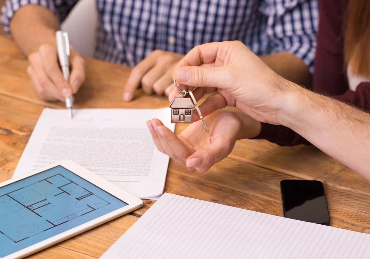 A person holding keys to a house on top of papers.